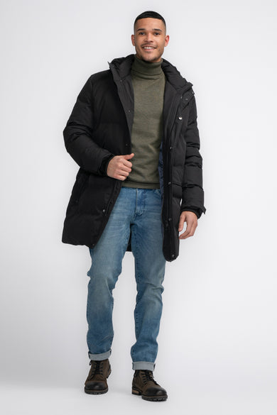 Lange zwarte jas van Petrol Industries, met een colbert en lichtblauwe jeans en bruine schoenen.
