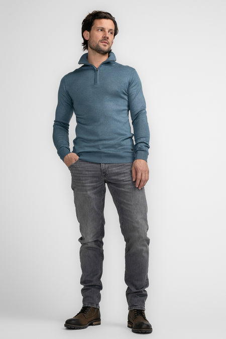 T-shirt bleu à col montant de Petrol Industries, avec des manches longues et des détails rayés, porté avec des jeans gris et des bottes brunes.
