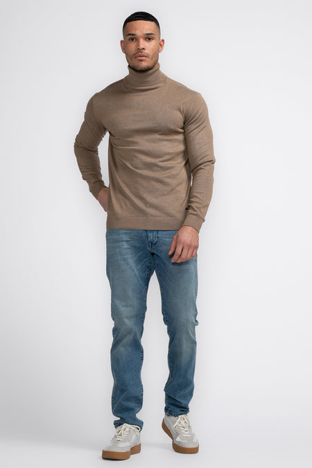 Beige rolkraagtrui van Petrol Industries®, gedragen met blauwe jeans en witte sneakers.