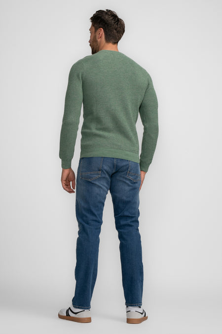 Pull vert à col rond de Petrol Industries, à manches longues et porté avec un jean bleu et des baskets blanches.