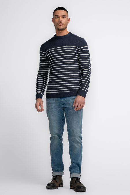 T-shirt bleu avec col rond de Petrol Industries®, à rayures horizontales blanches, associé à des jeans et des bottes.