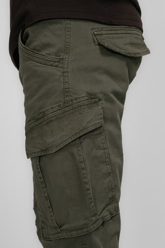 Pantalon de travail vert de Pet Petrol Industries, avec des po po et partie partie du vêtement brun partiellement visible sur un fond uniforme.