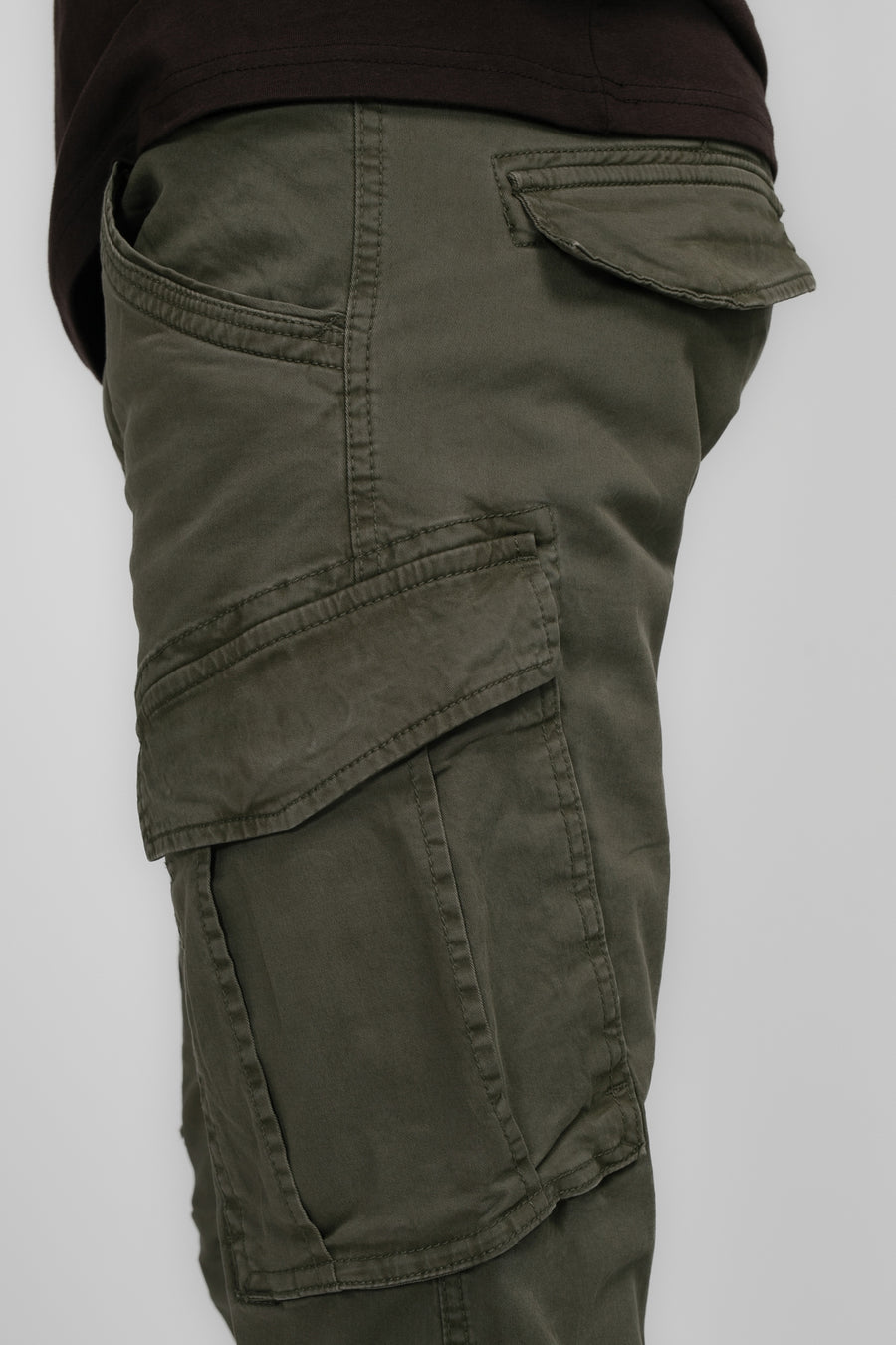 Pantalon de travail vert de Pet Petrol Industries, avec des po po et partie partie du vêtement brun partiellement visible sur un fond uniforme.