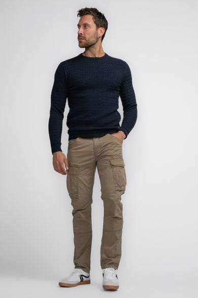 Bruine cargobroek van Petrol Industries® met grote zakken, gedragen met donkerblauwe trui en witte sneakers, volledig lichaamsvolledige weergave.