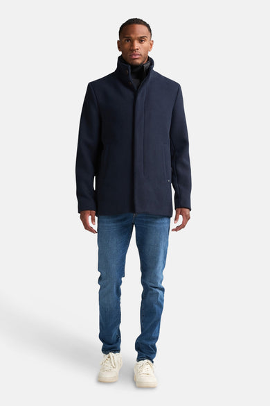 Blauwe lange jas van Petrol Industries® met een opstaande kraag en jeans en sneakers.