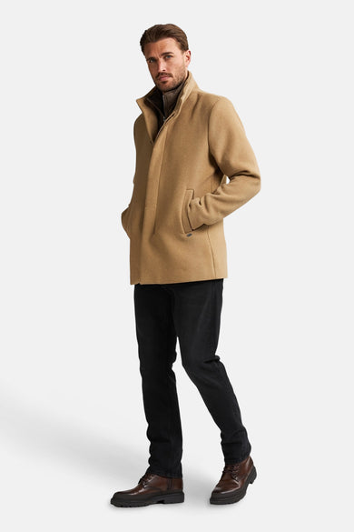 Manteau long beige de Petrol Industries, avec des jeans noirs et des chaussures marrons.