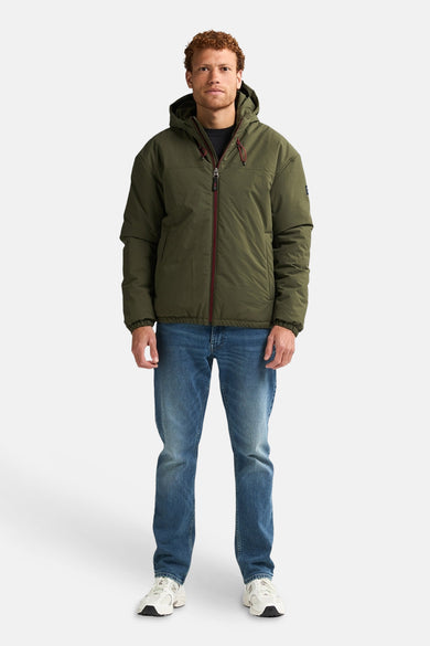 Groene korte jas van Petrol Industries, met een capuchon, gedragen met jeans en witte sneakers.
