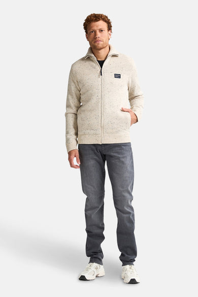 Korte ecru jas van Petrol Industries, met lange mouwen en een rits, gecombineerd met een grijze jeans en sneakers.