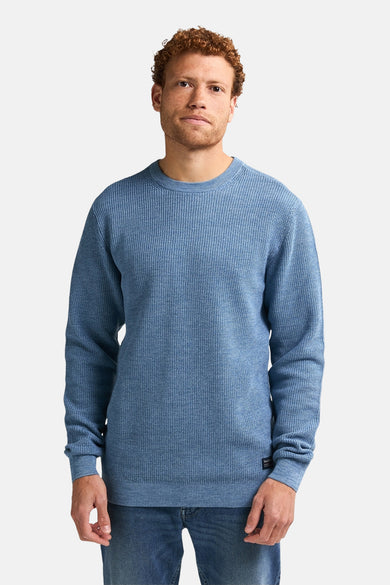 Blauwe trui met ronde hals van Petrol Industries, met een fijn wafelpatroon, gedragen met jeans.
