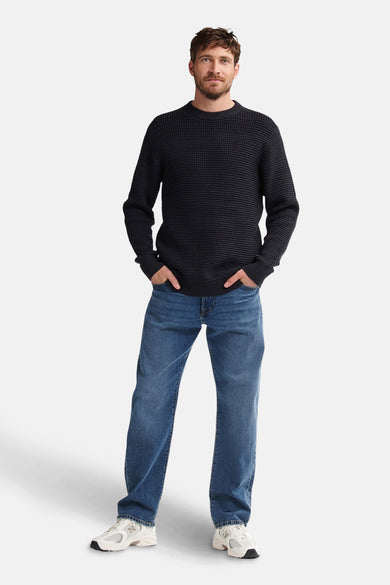 Pull noir avec col rond de Petrol Industries®, associé à des jeans bleus et des baskets blanches.