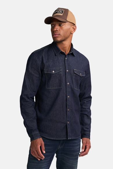 Donkerblauw denim overhemd met lange mouwen van Petrol Industries® met borstzakken en knoopsluiting, gecombineerd met jeans en een pet.