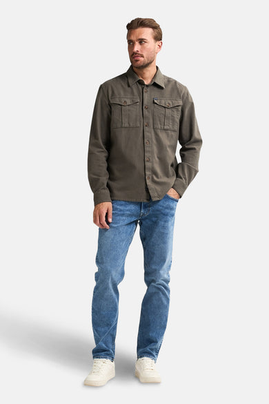 Groen overhemd met lange mouwen van Petrol Industries, met borstzakken en gedragen over een blauwe jeans en crèmekleurige sneakers.
