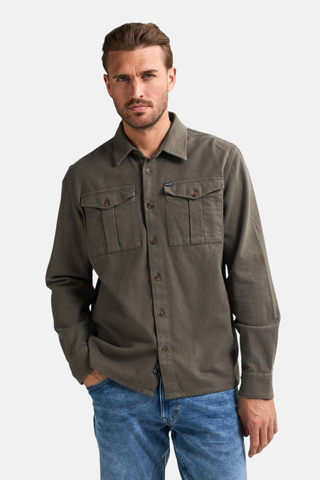 Groen overhemd met lange mouwen van Petrol Industries, met borstzakken en gedragen met een blauwe jeans.