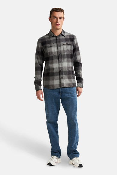 Chemise noire à manches longues de Petrol Industries®, avec un motif rayé et portée ouverte sur un jean.