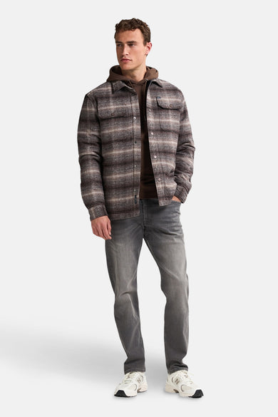 Bruine korte jas van Petrol Industries, met een geruit patroon en een bruine hoodie eronder, gecombineerd met grijze jeans en witte sneakers.
