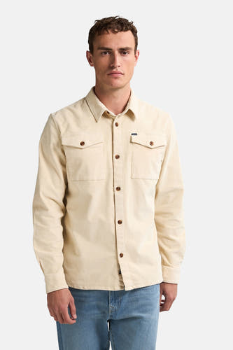 Beige overhemd met lange mouwen van Petrol Industries, met bruine knopen en twee borstzakken, gedragen met een blauwe jeans.
