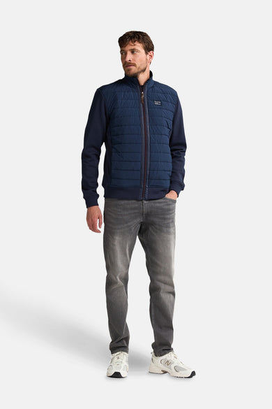 Blauwe korte jas van Petrol Industries, met ritssluiting en grijze jeans en witte sneakers.