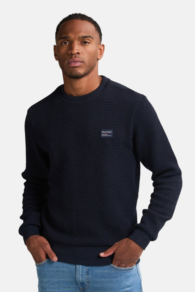 Blauwe sweater van Petrol Industries met een subtiele wafelstructuur en een ronde hals, gedragen met een spijkerbroek.

