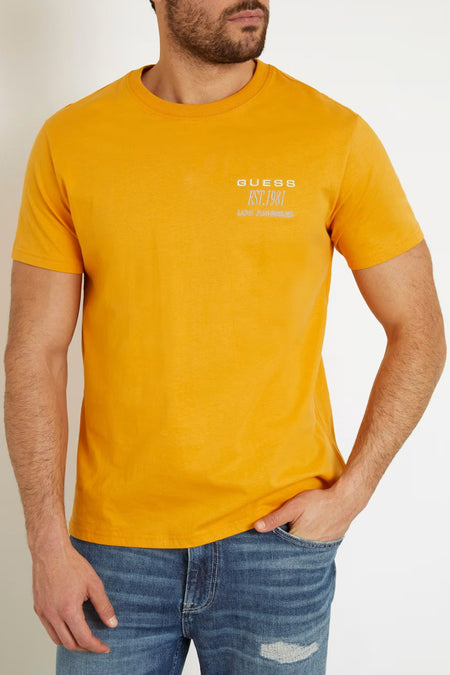 Oranje T-shirt van Guess met korte mouwen, opdruk op de borst en gedragen met een jeans.
