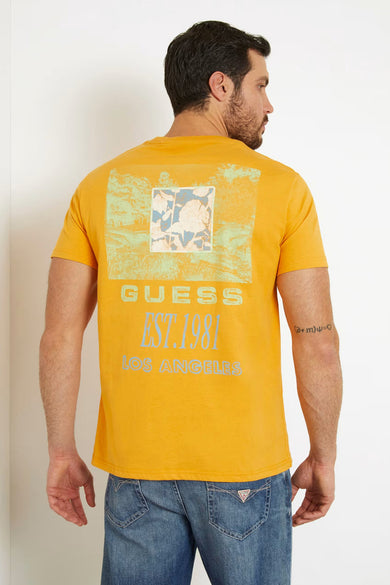 Oranje T-shirt van Guess met een rechthoekige print en de tekst 'Guess Est. 1981 Los Angeles' op de achterkant, gedragen met jeans.
