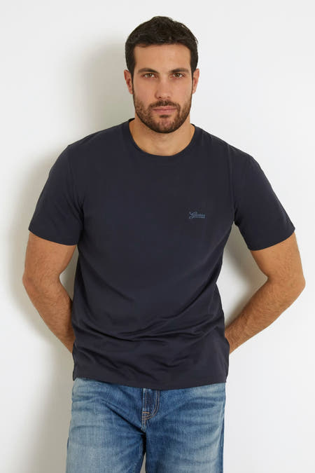 T-shirt bleu à manches courtes de Guess, on voit un tatouage sur le bras et le jean.
