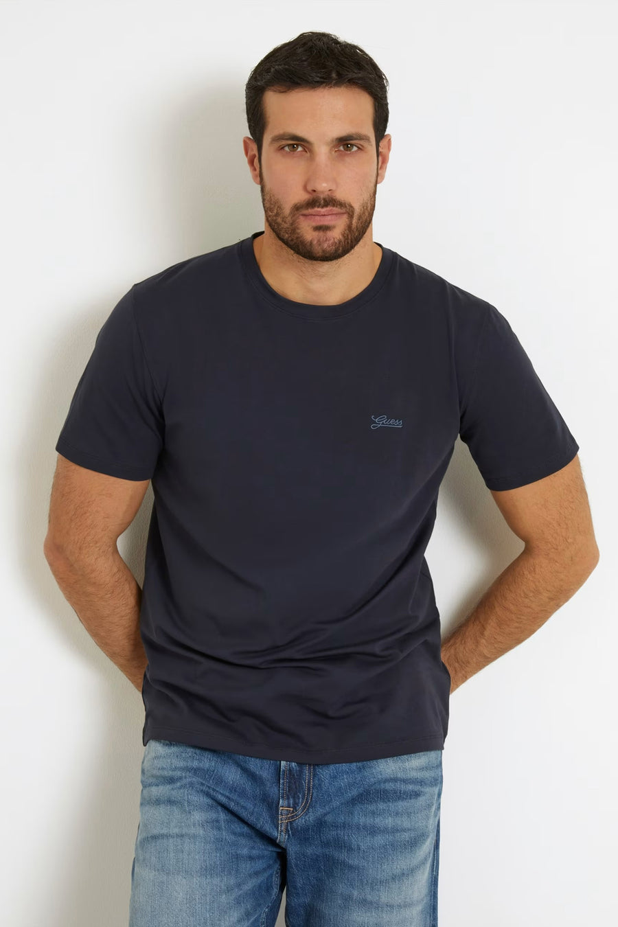 T-shirt bleu à manches courtes de Guess, on voit un tatouage sur le bras et le jean.