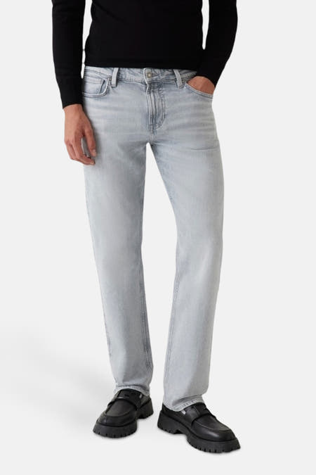 Jeans slim van lichtgrijze denim van Guess, gedragen met een zwarte trui en zwarte loafers.

