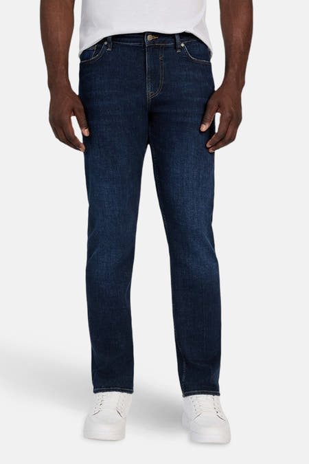 Jeans slim van donkerblauwe denim van Guess, gedragen met een wit T-shirt en witte sneakers.
