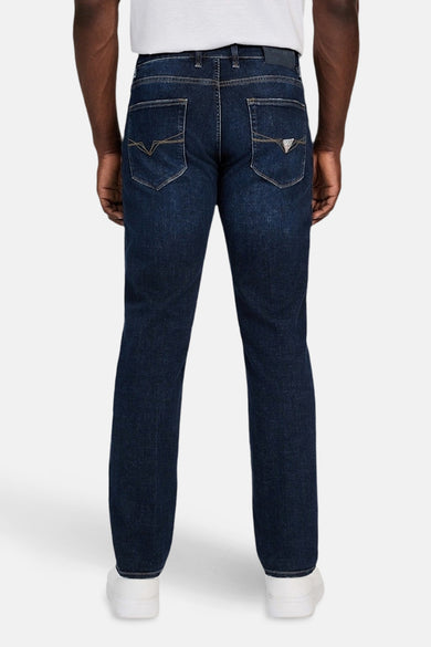 Slim jeans van donkerblauw denim van Guess, met zichtbare achterzakken en witte sneakers.
