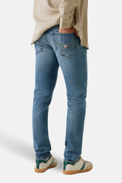 Jean droit en denim bleu moyen de Guess, avec des poches arrière et une chemise beige.
