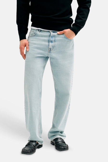 Jean droite bleu clair de Guess, porté par un mannequin avec un pull noir et des mocassins noirs.