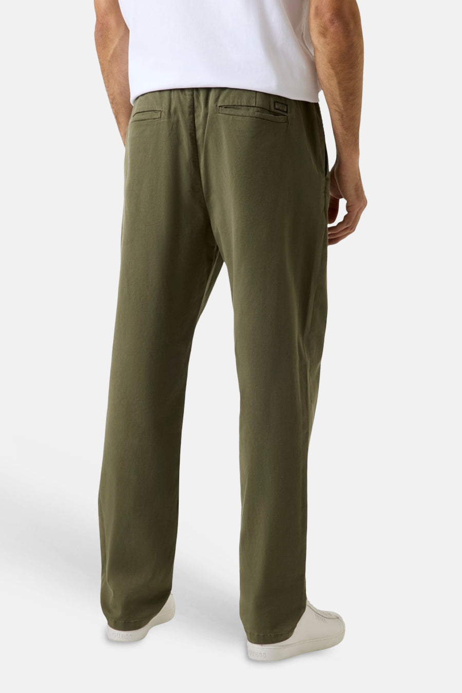 Pantalon vert Guess® avec taille élastique et poches arrière, porté par un homme avec un t-shirt blanc et des baskets blanches, vue de dos.