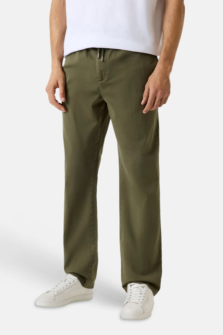 Groene broek van Guess met trekkoord in de taille, gedragen met wit T-shirt en witte sneakers.