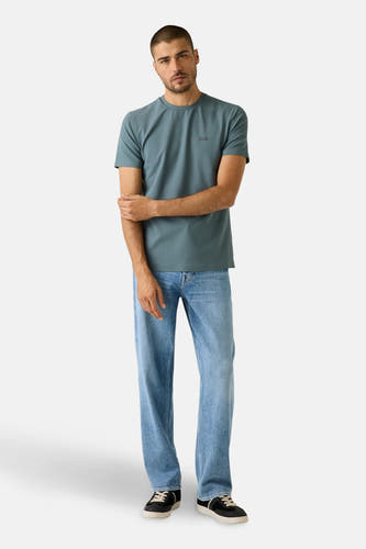 T-shirt bleu à manches courtes de Guess, porté avec un jean décontracté et des baskets noires.