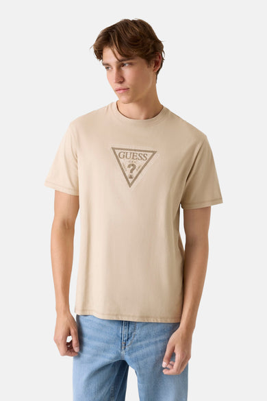 Beige T-shirt met korte mouwen van Guess, met een grafische print op de voorkant, gedragen met jeans.
