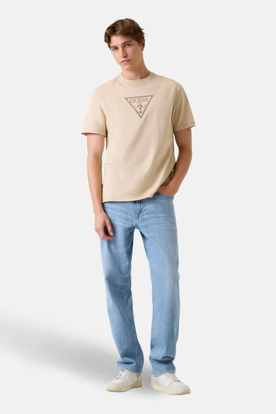 Beige T-shirt met korte mouwen van Guess, met een logo op de borst, gecombineerd met jeans en sneakers.