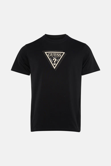 T-shirt noir de Guess, avec un imprimé graphique sur la poitrine, porté avec un jean déchiré et des baskets.