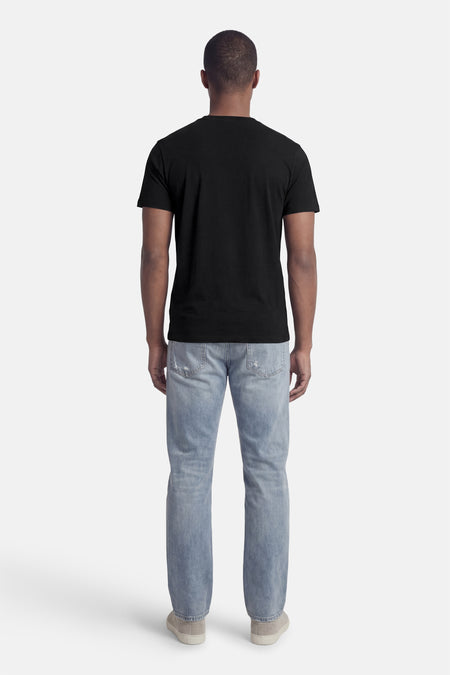 T-shirt noir Guess®, à manches courtes, porté avec un jean bleu et des chaussures grises, vu de dos.