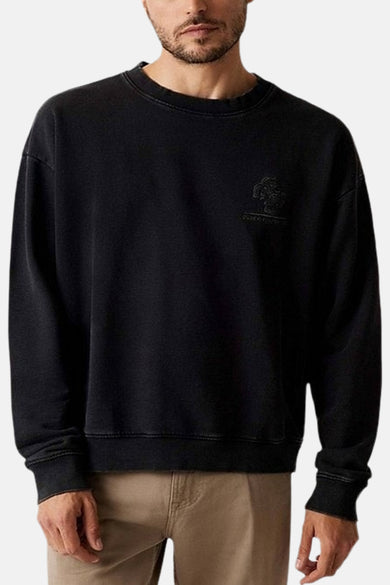 Zwarte sweater met ronde hals van Guess, met klein logo-embleem op de borst, gedragen met kaki broek.