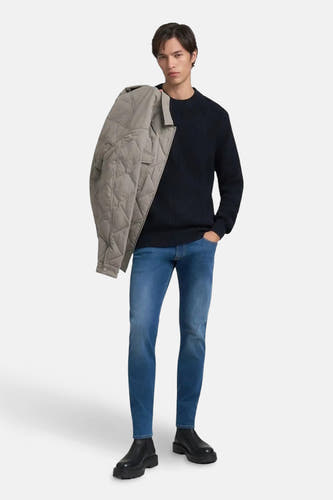 Slim jeans in middenblauw denim van REPLAY, met een model die een jas over zijn schouder draagt.