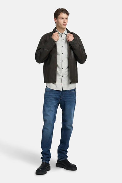 Blauwe rechte jeans van REPLAY, gecombineerd met een gestreept overhemd en een bruine leren jas.