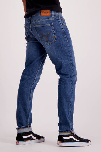 Jean slim en denim bleu de Le Fabuleux Marcel de Bruxelles, avec des poches rabattues et des baskets noires.