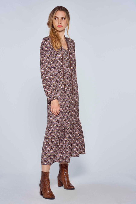 Lang kleedje met multicolor bloemenprint van Le Fabuleux Marcel de Bruxelles, voorzien van ritsvoorkant en wijd uitlopende zoom, gedragen met bruine hakken.
