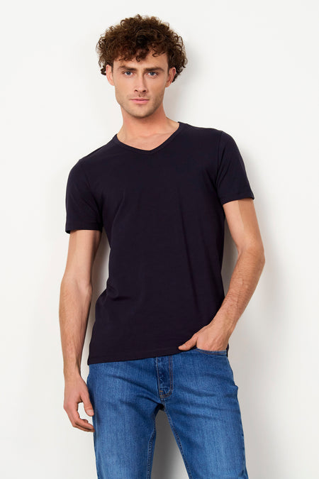 T-shirt noir de Le Fabuleux Marcel de Bruxelles avec col en V, porté par un homme en jean bleu.