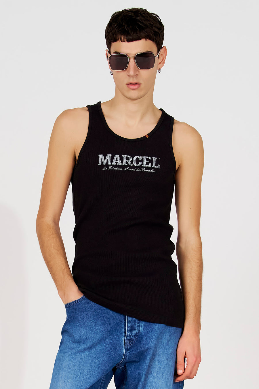 Zwarte tanktop van Le Fabuleux Marcel de Bruxelles, met tekstprint op de borst, gedragen met blauwe jeans en zilverkleurige zonnebril.
