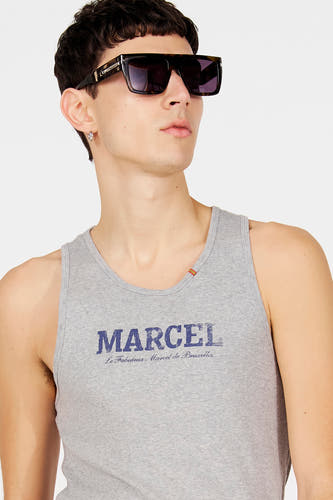 Grijze tanktop van Le Fabuleux Marcel de Bruxelles, met blauwe tekstprint op de voorkant, gedragen met een zonnebril en zilveren oorbel.
