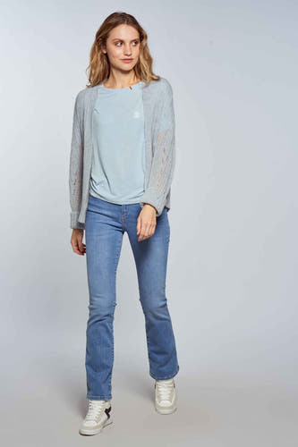 Jean bootcut bleu clair de Le Fabuleux Marcel de Bruxelles, porté avec un cardigan gris et des baskets blanches.