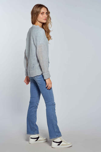 Jean bootcut bleu clair de Le Fabuleux Marcel de Bruxelles, porté avec un pull gris et des baskets blanches.
