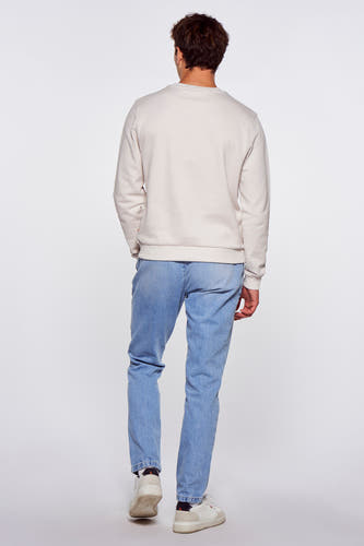 Jeans en denim bleu clair de Le Fabuleux Marcel de Bruxelles, combinés avec un pull beige et des baskets blanches, vus de dos.