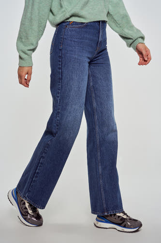 Jean bleu marine large de Le Fabuleux Marcel de Bruxelles, avec une chemise verte claire et des baskets argentées.